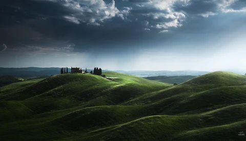Tuscan villa with cypress trees on rolling green hills under dramatic cloudy sky.