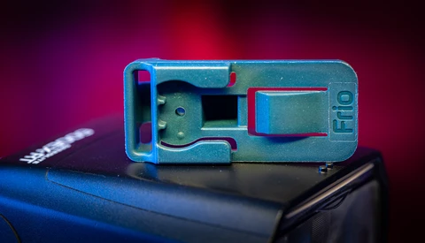 Disassembled blue and teal mechanical camera or device component against a dark background with magenta lighting.