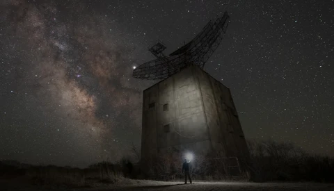 Silhouetted figure standing before an abandoned windmill beneath the Milky Way.