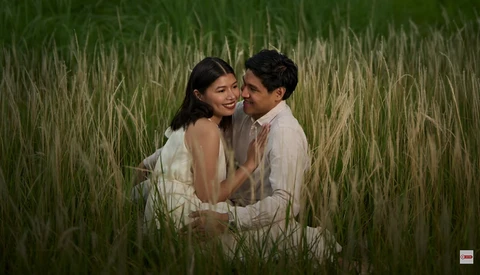 Couple embracing in a tall grain field during golden hour with soft, warm lighting.