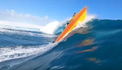 Surfer riding an orange and yellow surfboard down the face of a large blue wave.