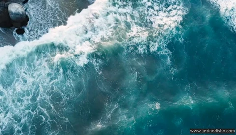 Aerial view of ocean waves crashing on a beach with white foam and turquoise water.