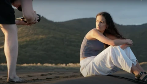 Woman sitting on beach with mountains in background during golden hour shoot.