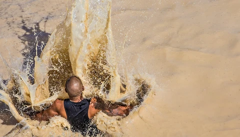 Person wading through turbid water with powerful wave splash creating dramatic white foam around them.