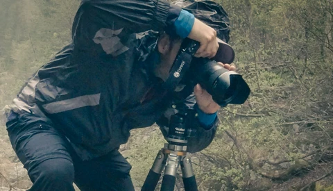 Overhead view of photographer operating a camera mounted on a tripod in an outdoor grassy setting.