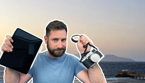 Man holding camera gear against ocean backdrop at sunset.