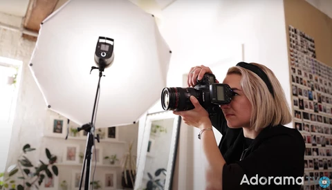 Photographer holding a camera with telephoto lens in a studio with large softbox lighting setup.