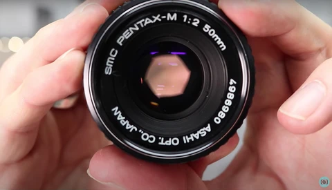SMC Pentax-M 1:2 50mm lens held in hands, showing aperture blades and front element.
