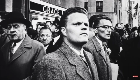 Black and white photograph of men in suits and hats in a crowded street scene with signage visible in background.