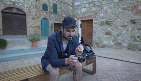 Photographer holding a mirrorless camera while seated outdoors in a historic stone courtyard.