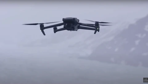 Quadcopter drone flying against an overcast sky with gray clouds in the background.