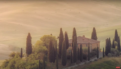 Tuscan villa surrounded by cypress trees in rolling hills at golden hour.