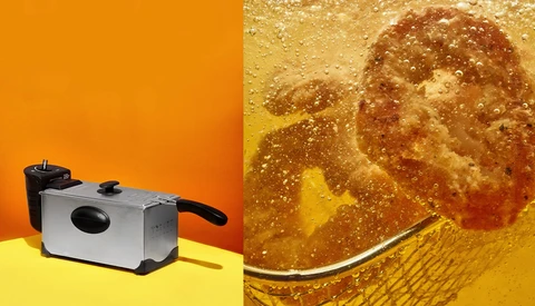 Deep fryer with stainless steel body and black handles on yellow surface against orange background.