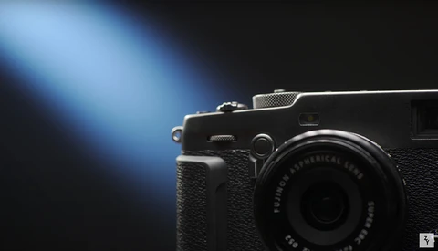 Compact rangefinder camera with textured black body positioned against a dark background with blue directional lighting.