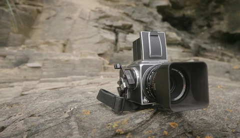 Vintage medium format camera with lens hood positioned on textured stone surface.