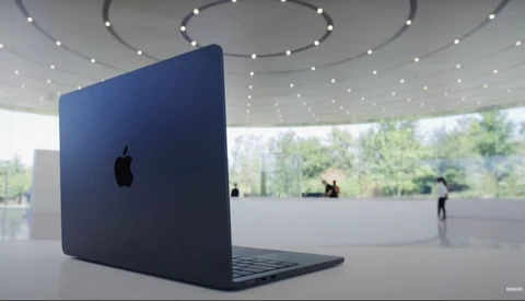 Dark blue MacBook laptop displayed at an angle in a minimalist interior space with curved ceiling and recessed lighting.