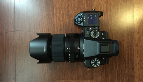 Mirrorless camera with attached lens and lens hood on wooden surface, overhead view.