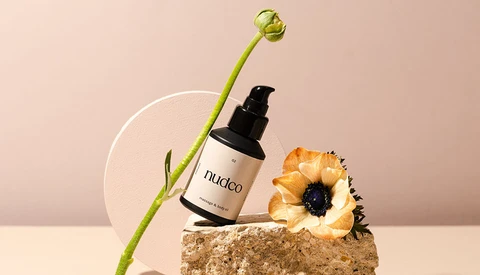 Cosmetic product photography featuring a spray bottle with natural elements on textured stone.
