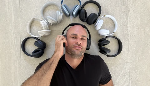 Man wearing black headphones surrounded by nine other headphones arranged in a circle on a light tile floor.