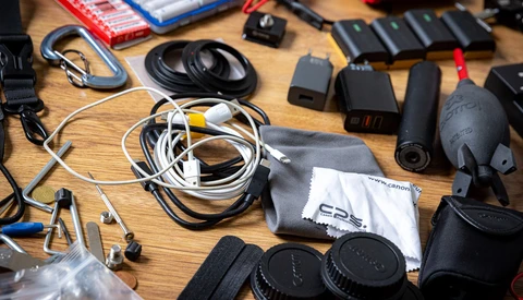 Photography gear and equipment organized on a wooden table, including headphones, cables, lens caps, and drone components.