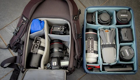 Photography gear organized in a burgundy backpack and blue storage insert, including camera body, lenses, and accessories.