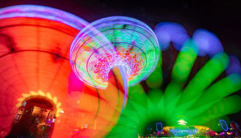 Nighttime carnival or fair scene with glowing red Ferris wheel on left and neon green inflatable structures on right against dark sky.
