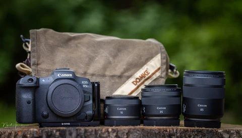Canon EOS R5 camera body with four RF-mount lenses and a canvas camera bag arranged on a wooden surface.