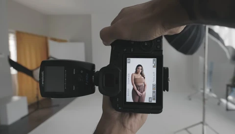 Photographer's hand holding a camera displaying a portrait of a woman on its rear LCD screen during a studio shoot.