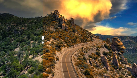 Winding mountain road with dramatic golden sunset sky and forested hillside.