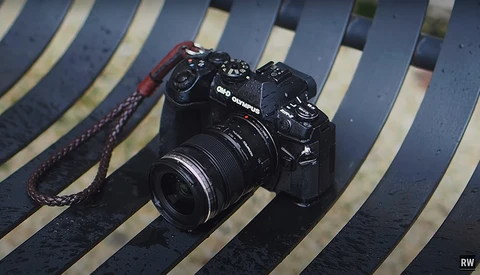 Black mirrorless camera with attached lens on striped blue and white background with red camera strap.