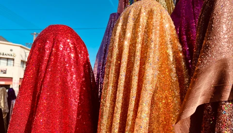 Vibrant sequined fabrics in red, gold, and burgundy draped and displayed outdoors in bright sunlight.