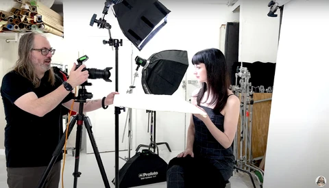Cinematographer operating a camera on tripod while filming a subject in a studio with professional lighting setup.