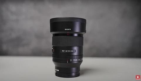 Sony FE 1.4/35 GM prime lens with hood mounted, displayed against neutral gray background.