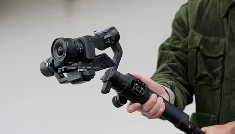 Videographer holding a gimbal-stabilized camera rig with mounted lens and monitor.