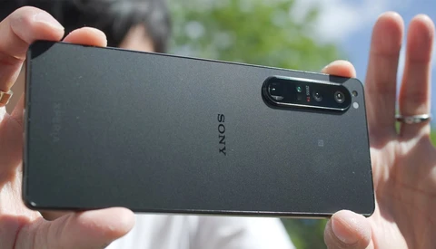 Sony smartphone held in hands outdoors, displaying rear camera module with multiple lenses against blurred green background.