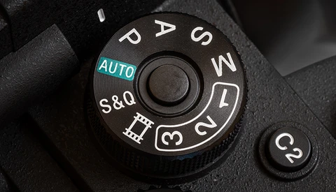 Close-up of a camera mode dial showing AUTO, P, S, A, M, and other exposure modes with manual focus settings.