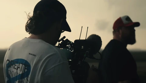 Cinematographer operating a camera rig during golden hour outdoor shoot with crew members visible in background.