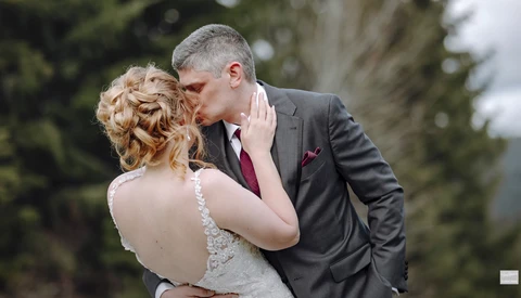 Bride and groom kissing outdoors, with bride wearing beaded backless gown and groom in charcoal suit.