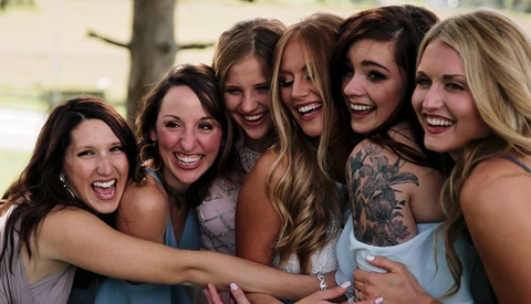 Six women smiling and posing together outdoors in natural daylight.