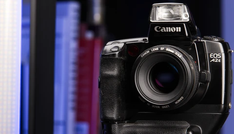 Canon EOS 1V film camera with battery grip attached, positioned against blurred blue and dark background.