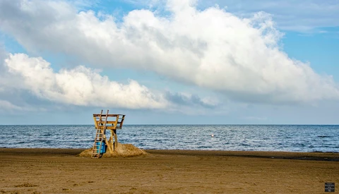 Abandoned yellow lifeguard tower standing alone on an empty beach under a blue sky with white clouds.