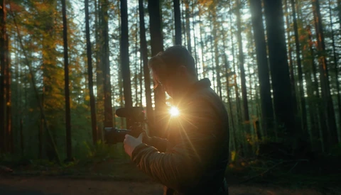 Photographer holding a camera with bright sunlight flaring through the lens in a forest setting.