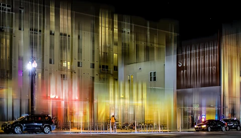 Modern building facade illuminated with vertical neon light strips in red, yellow, and blue at night.