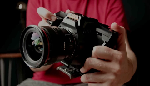 Photographer in pink shirt holding a vintage rangefinder camera with wide-angle lens and flash attachment.