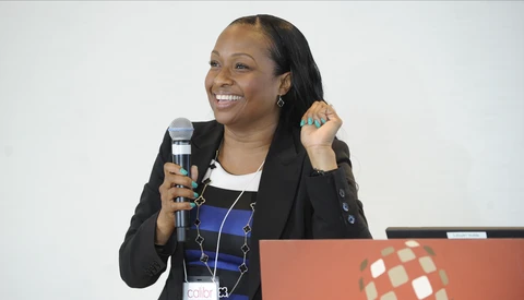 Woman speaking at a conference with microphone, wearing black blazer over striped top.