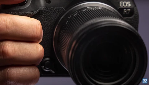 Photographer's hand holding Canon EOS mirrorless camera with attached lens in close-up view.