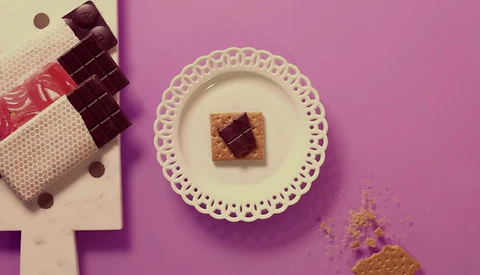 Styled flat lay with chocolate squares on a decorative plate and wrapped candies on a split pink and cream background.
