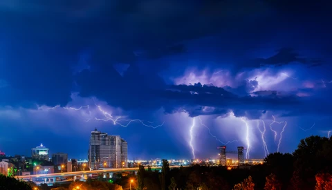 Thunderstorm with multiple lightning bolts striking over an illuminated city skyline at night.