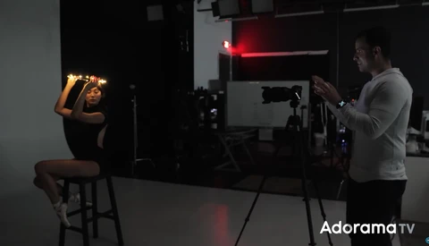 Photographer shooting a portrait of a seated subject in a studio with professional lighting setup.