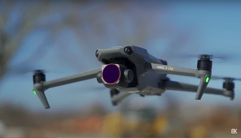 DJI Mavic 3 Classic drone in flight with folded landing arms and camera visible against blurred background.